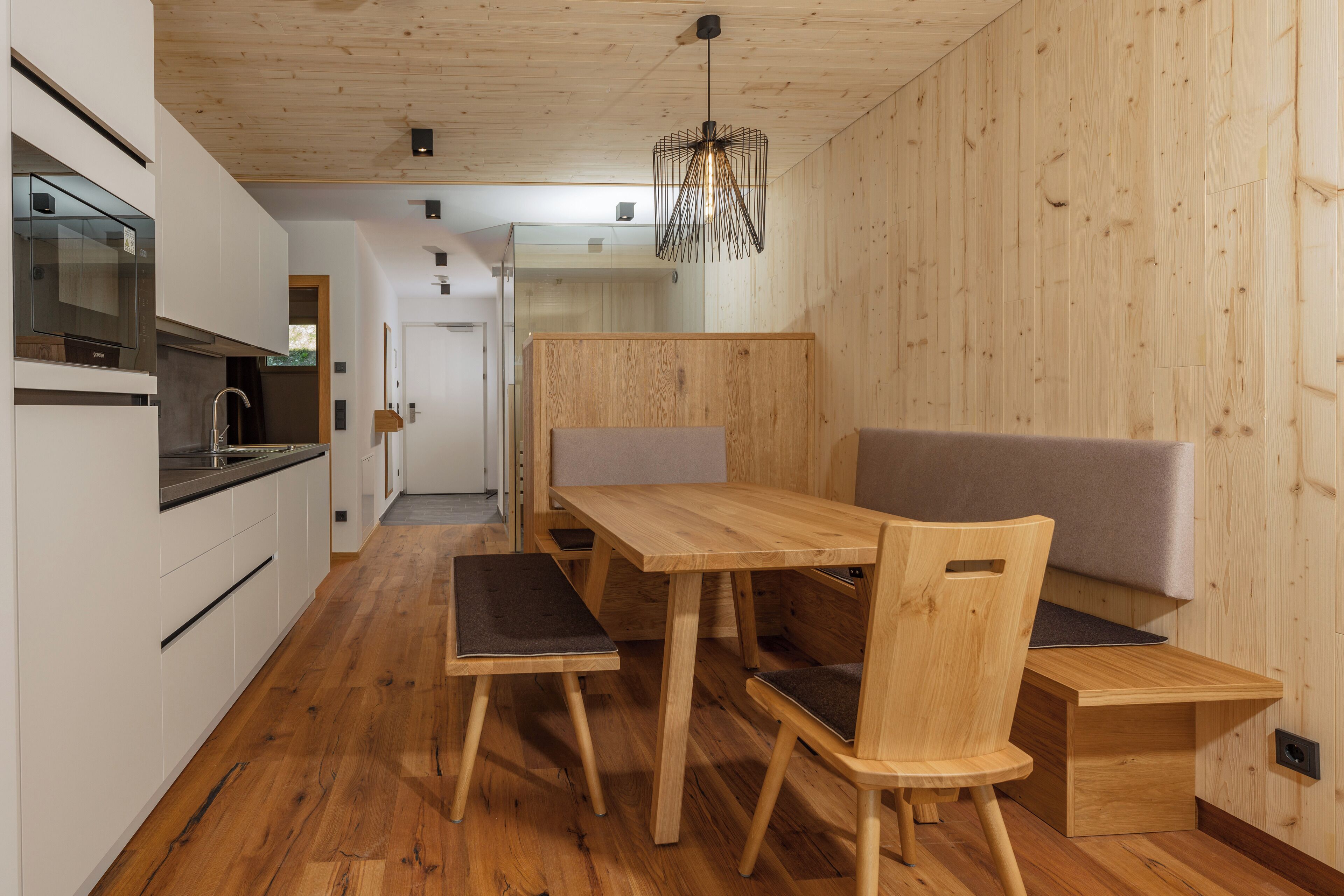 Eine moderne Küche mit Holzboden, integriertem Backofen und Essbereich mit Holztisch und Stühlen.