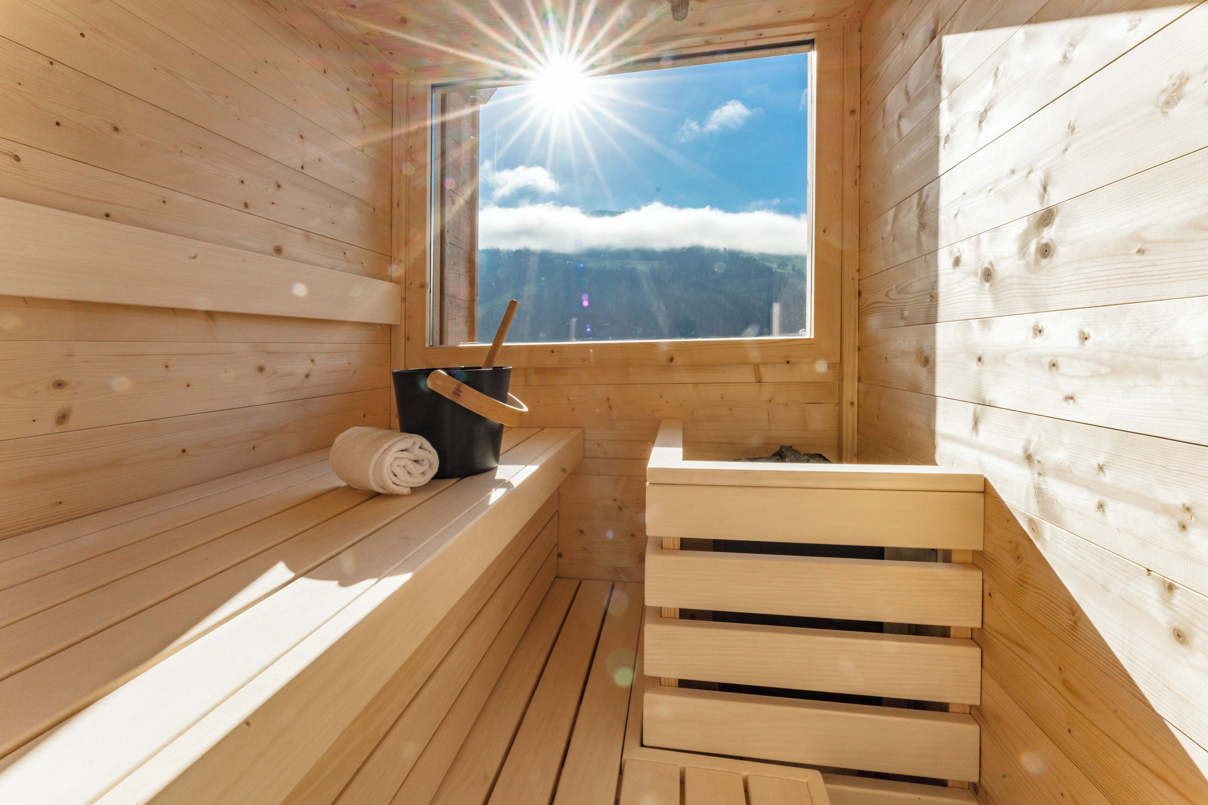 A wooden sauna with a bench, a bucket, and a towel.