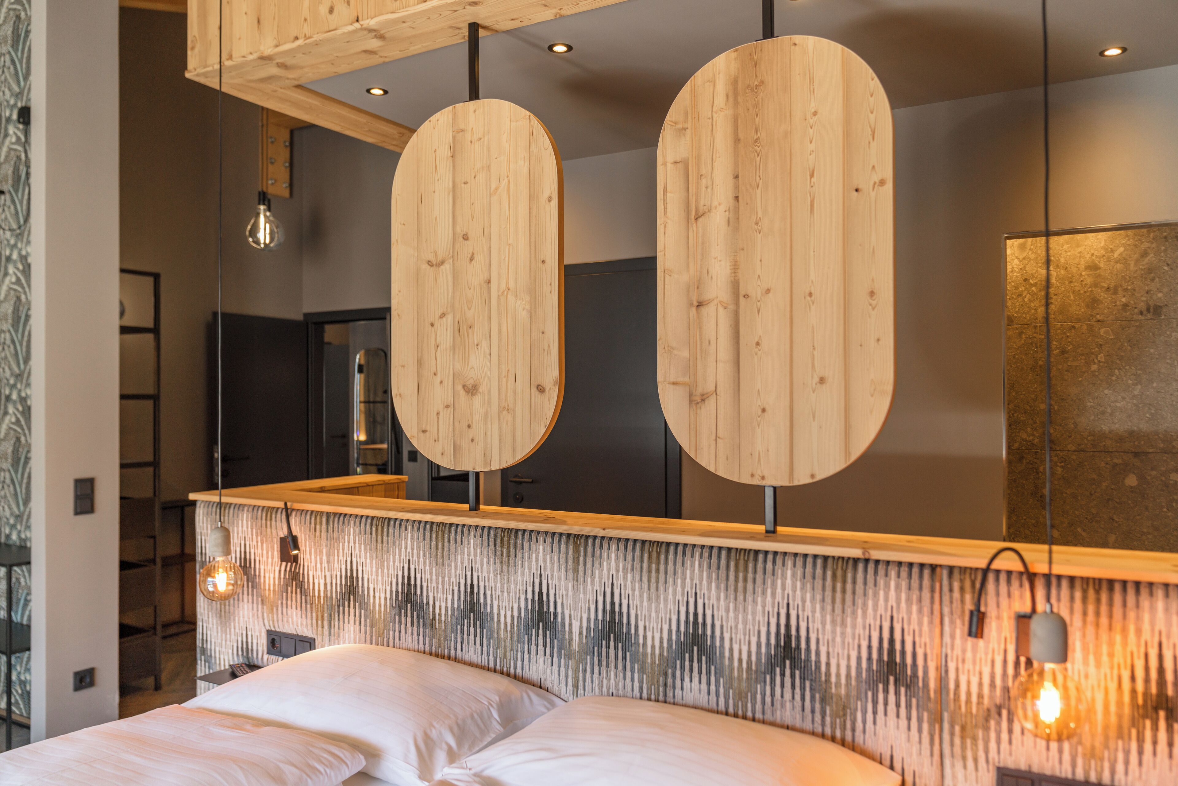 Ein modernes Schlafzimmer mit Holz-Kopfteil, einem großen Spiegel und Pendelleuchten.