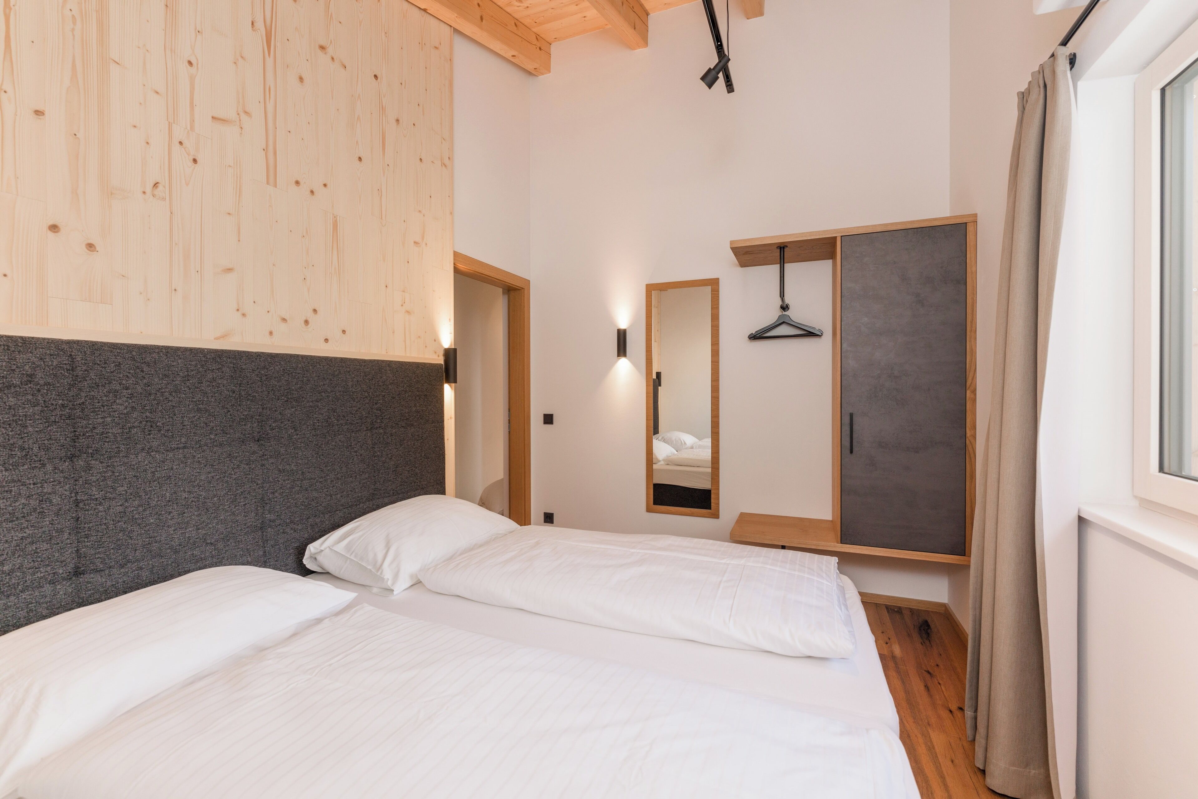 Ein Schlafzimmer mit einem Bett, einem Kleiderschrank, einem Spiegel und einem Fenster.