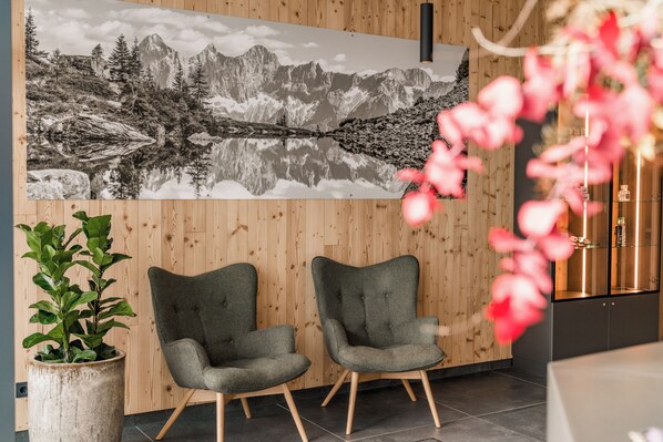 Una habitación con pared de madera, dos sillones grises tapizados, un cuadro grande de un paisaje montañoso en blanco y negro, y una planta en maceta.