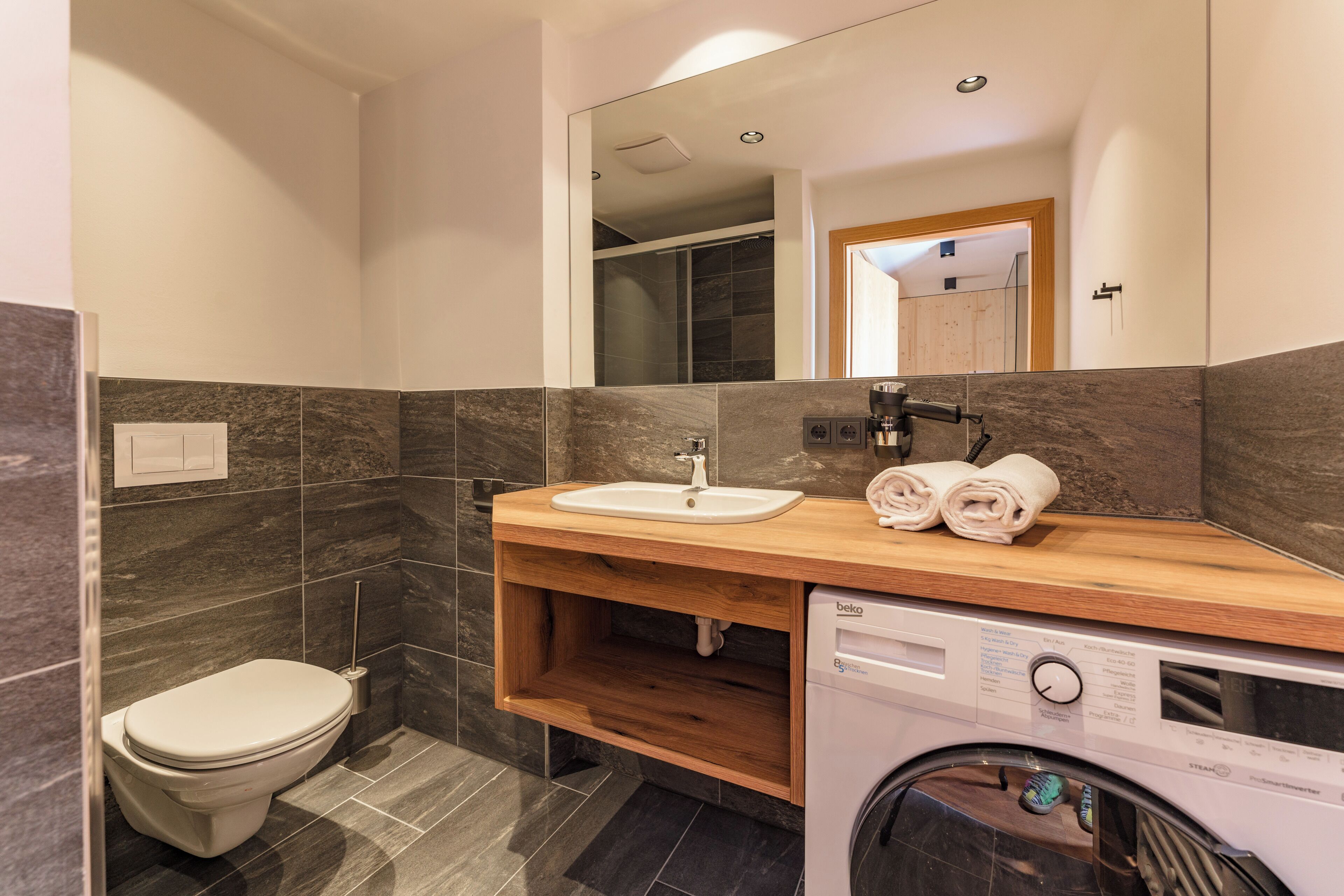 A modern bathroom with a toilet, sink, mirror, and built-in washing machine.
