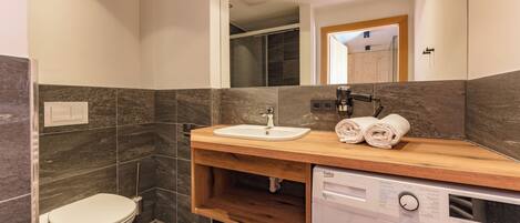 A modern bathroom with a toilet, sink, mirror, and built-in washing machine.