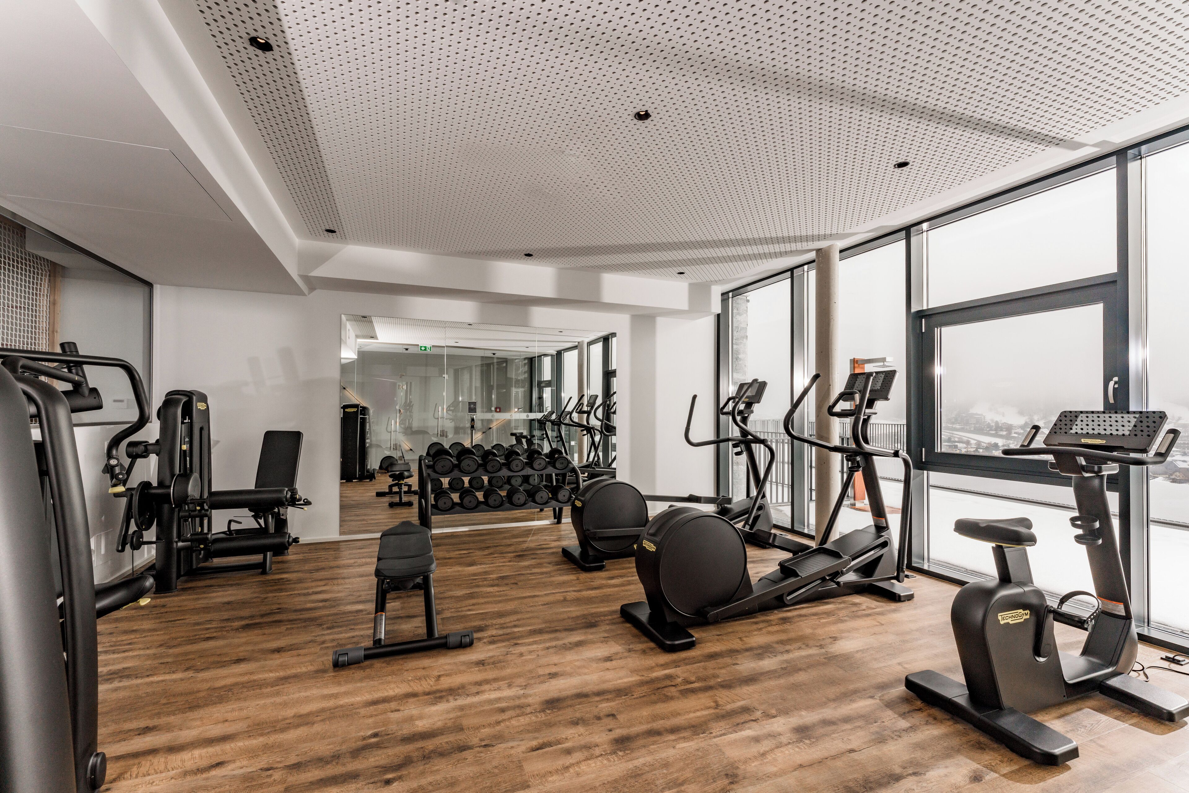 A modern gym with cardio equipment, weight machines, and a mirror wall.