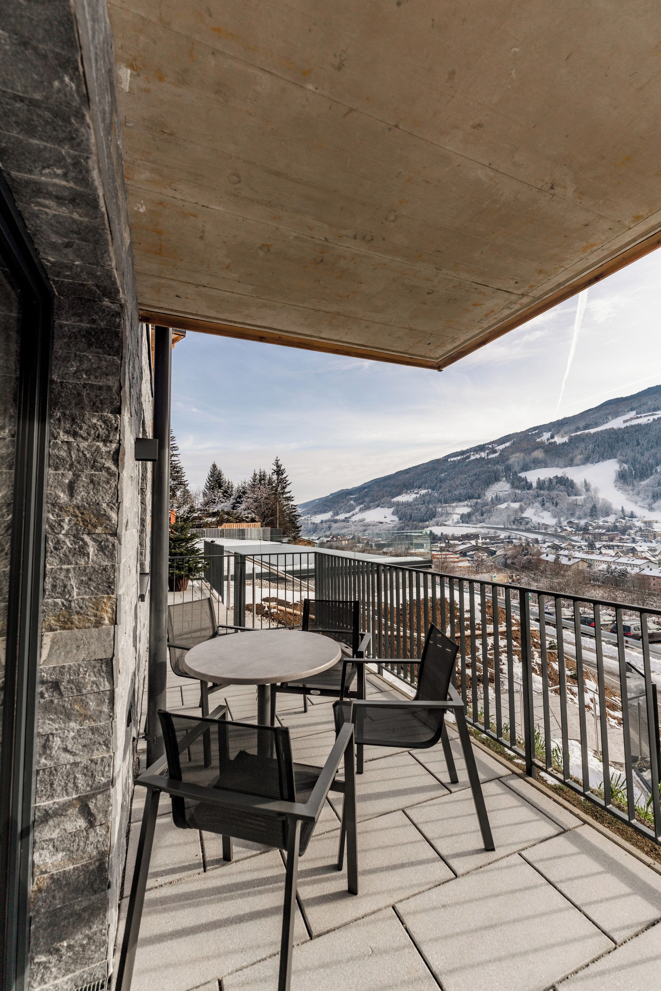 Un balcón con mesa y sillas, con vista a un paisaje nevado y un pueblo.