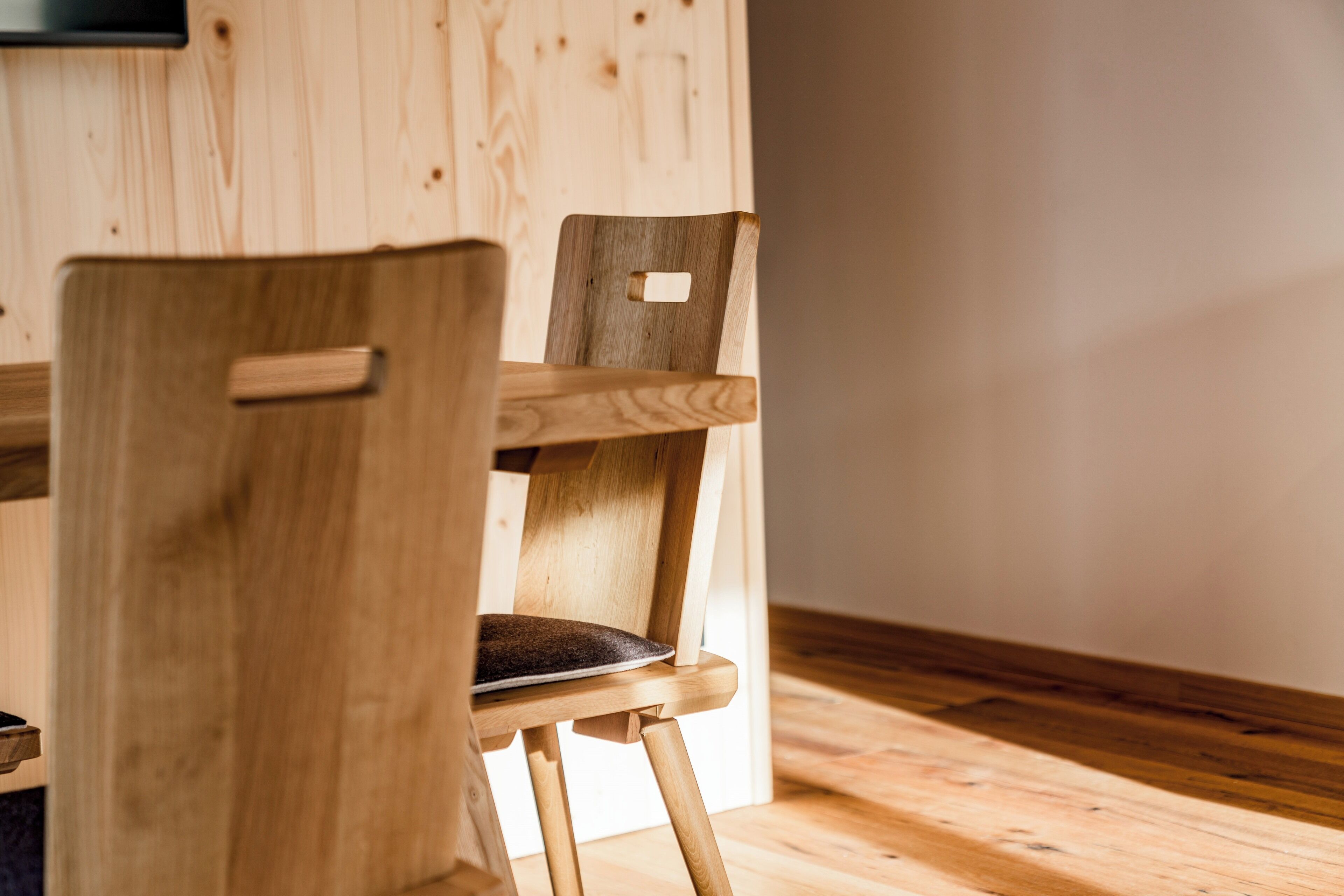 A wooden chair with a cushioned seat and backrest, positioned in a room with wooden flooring and walls.