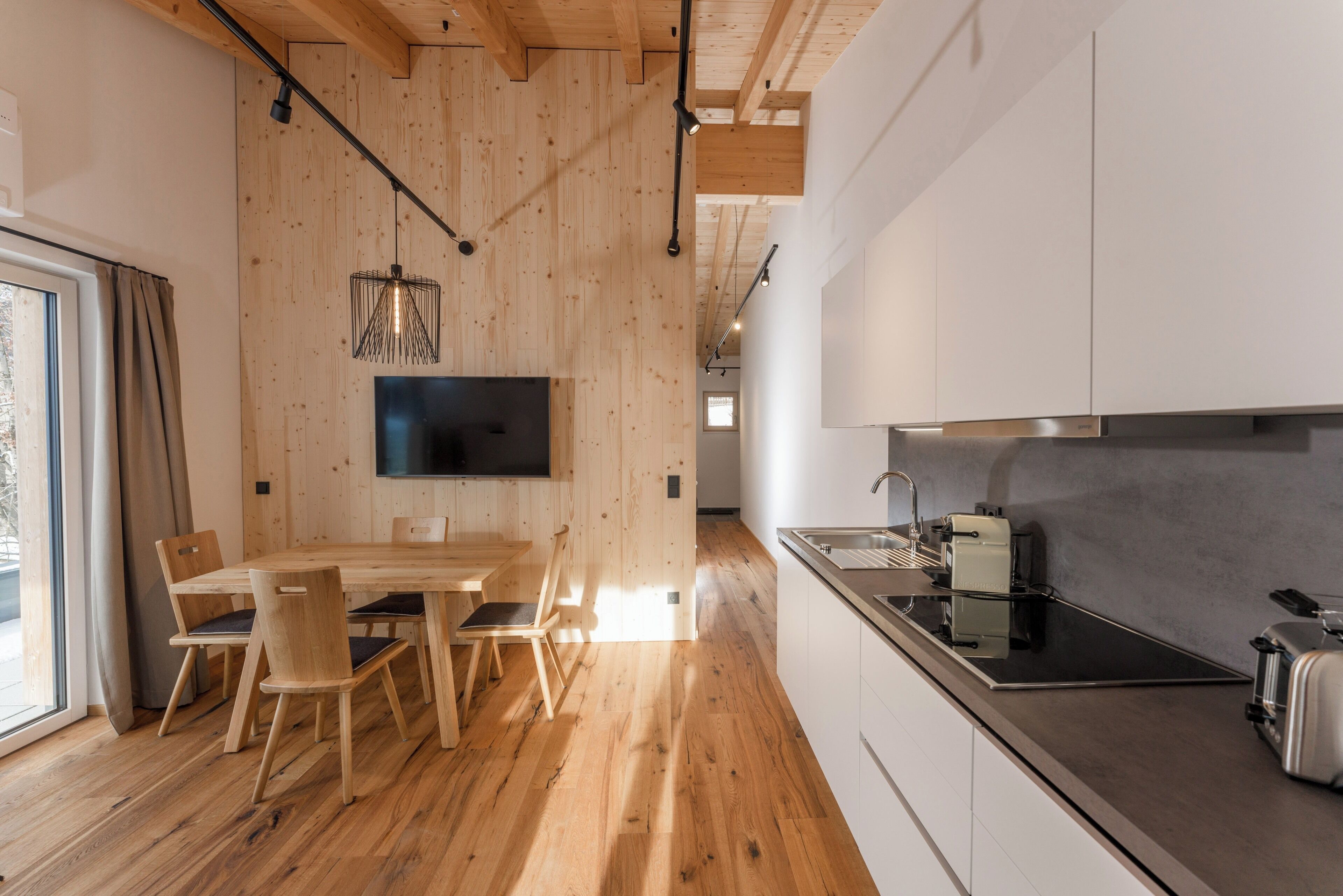 A modern kitchen with wooden flooring, a dining area with a table and chairs, and a built-in TV.