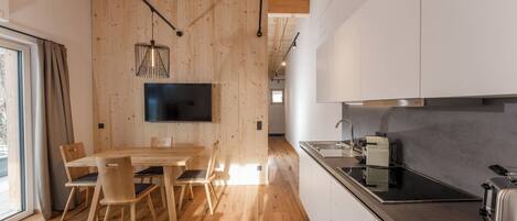 A modern kitchen with wooden flooring, a dining area with a table and chairs, and a built-in TV.