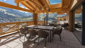 A wooden deck with a table and chairs, overlooking a mountainous landscape.