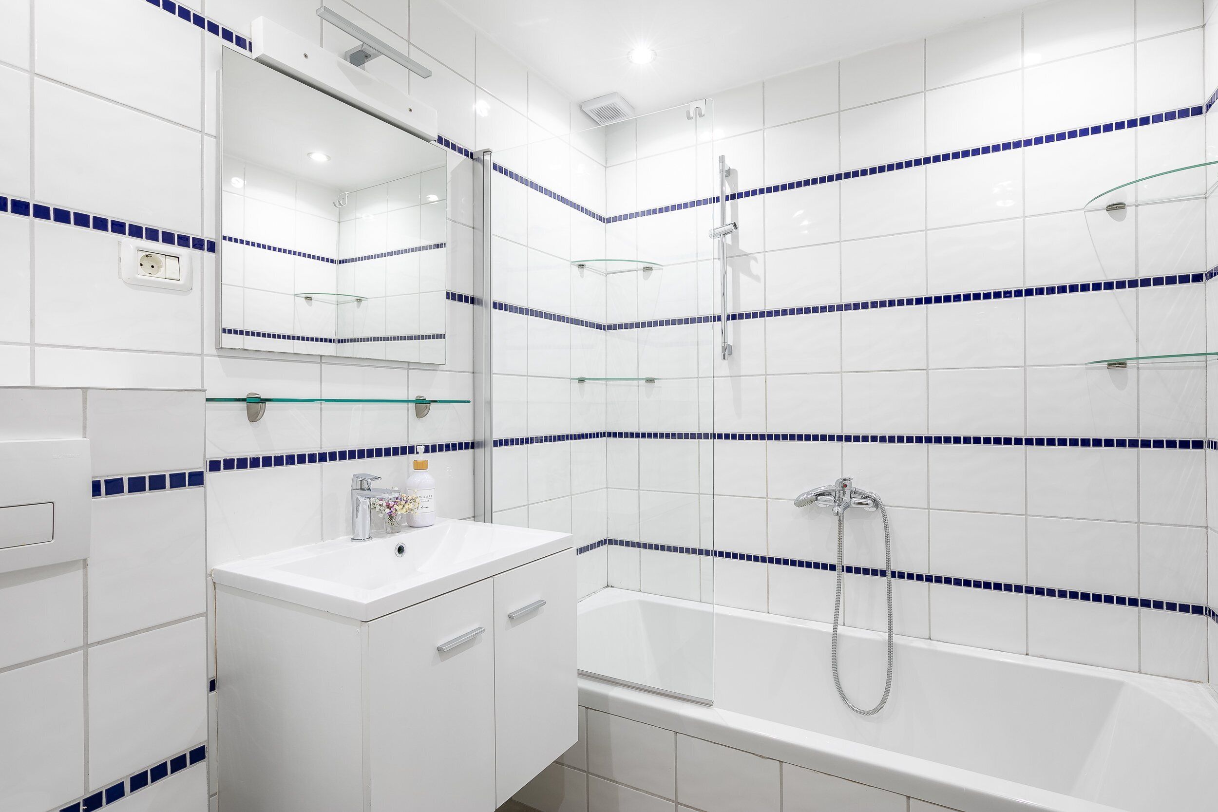 Un baño moderno con azulejos blancos, cabina de ducha de vidrio y tocador blanco con espejo.