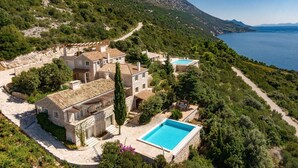 A hillside villa with a swimming pool, surrounded by lush greenery and overlooking a lake. - Stone Houses Dingač (Orebic)