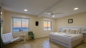 A bedroom with a large bed, a chair, a small table, and two windows offering a view of the sea. - Stone Houses Dingač (Orebic)