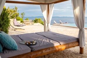Ein Bett mit Meerblick, ein Hängesessel und eine Liege am Pool.