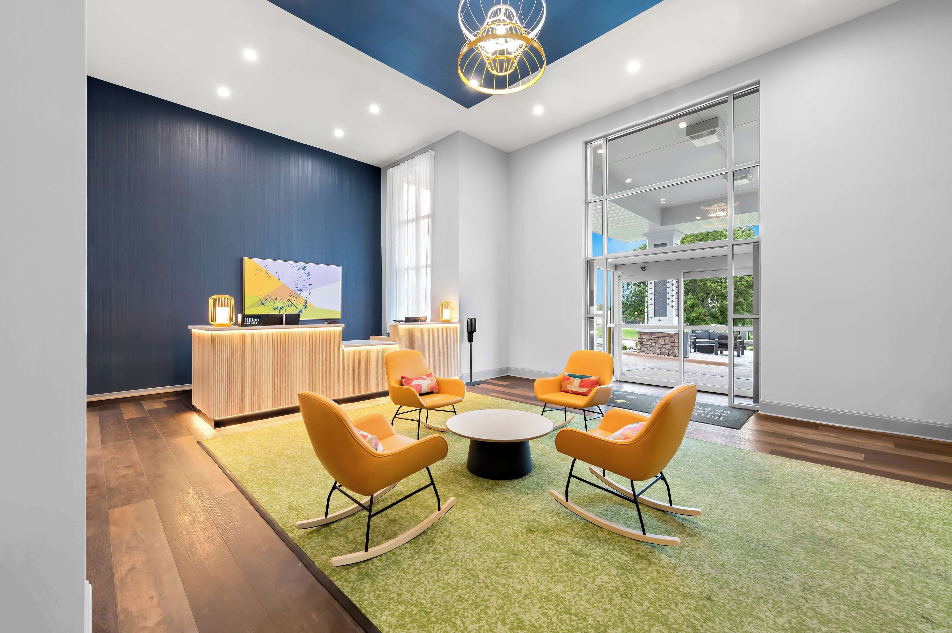 A modern conference room with a green carpet, orange rocking chairs, and a round table.