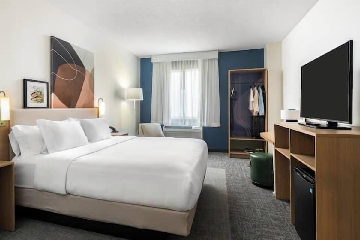 A hotel room with a bed, bedside tables, a TV, a wardrobe, and a window with curtains.