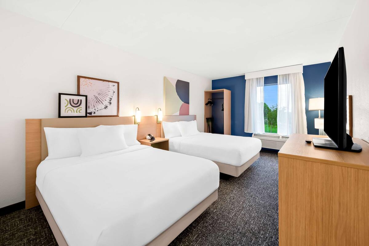 A hotel room with two beds, a desk, a TV, and artwork on the wall.