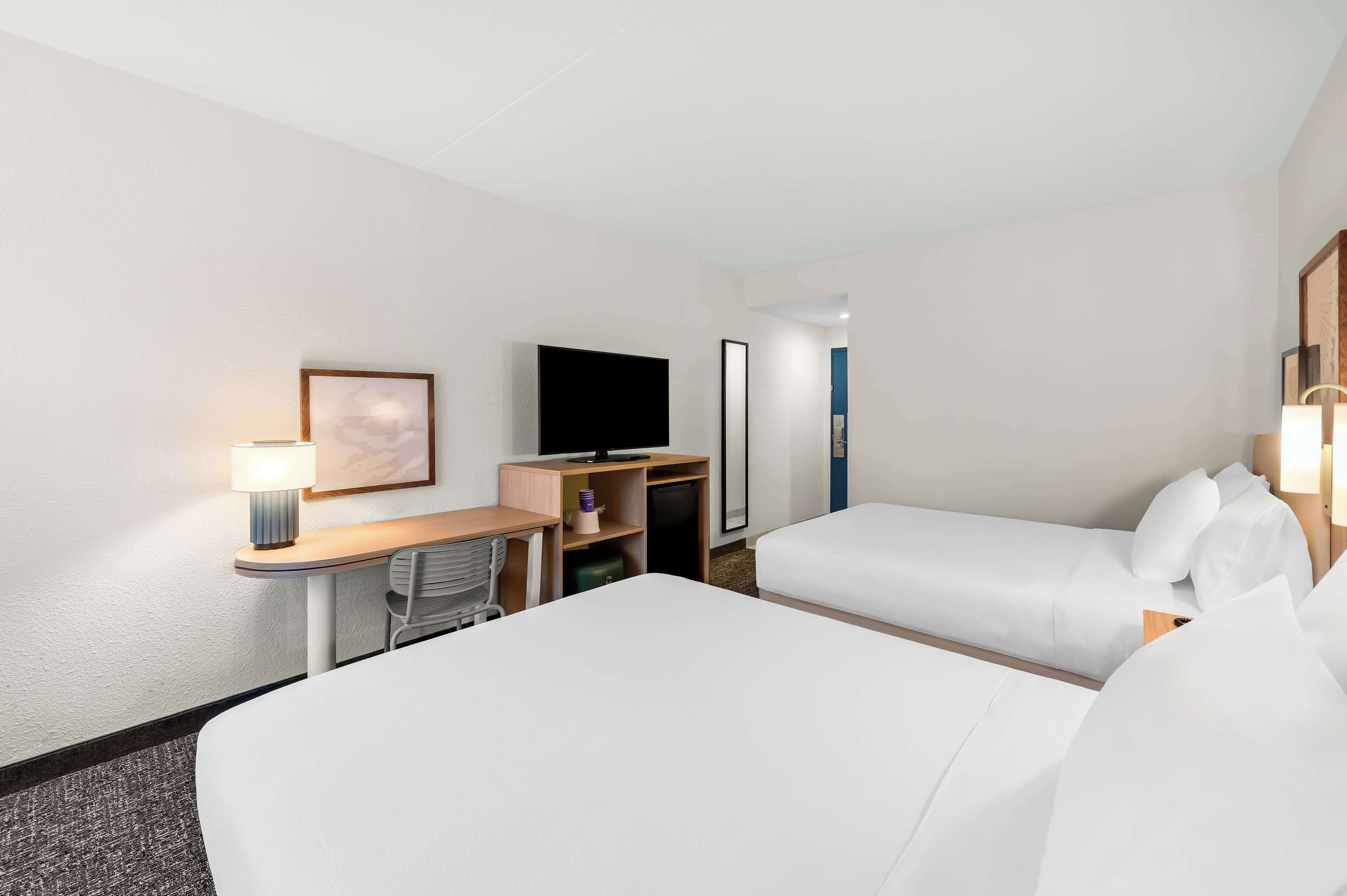 A hotel room with two beds, a desk with a lamp, a flat-screen TV, and a small seating area.