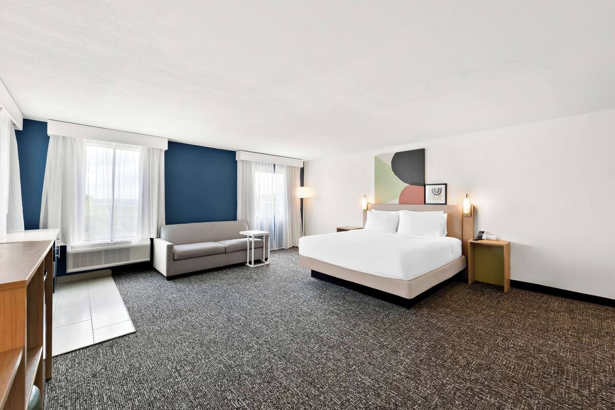 A hotel room with a large bed, a sofa, a desk, and a small table.
