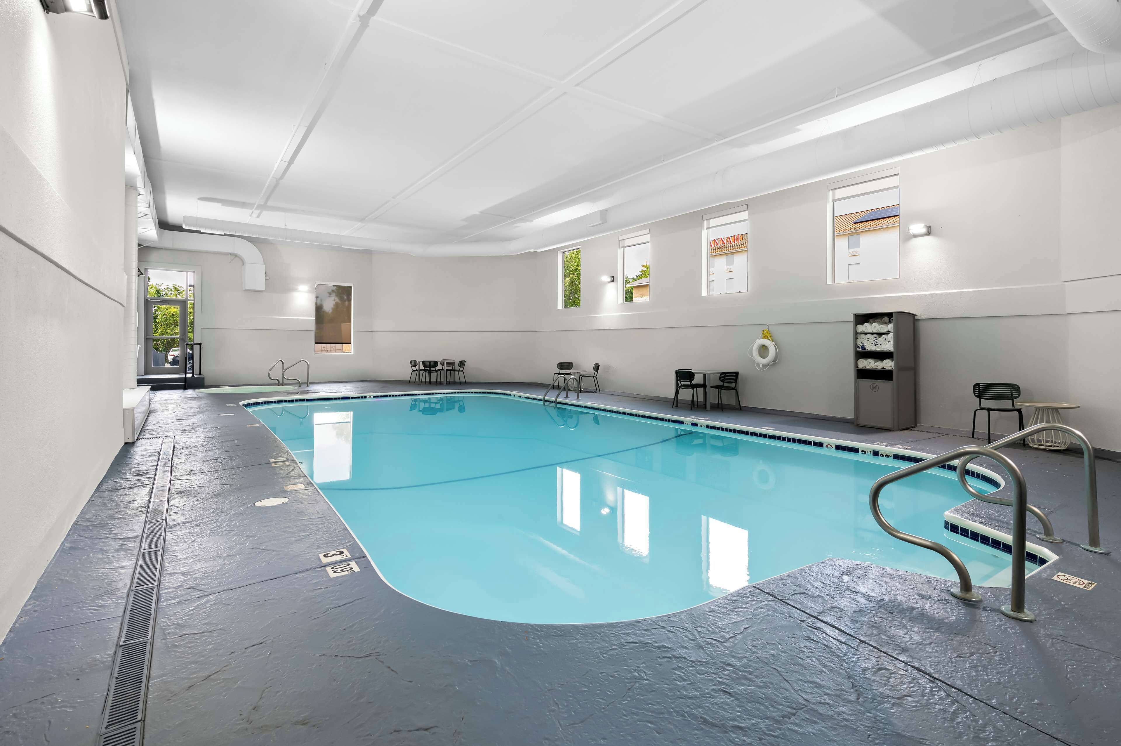 An indoor swimming pool with clear water, a metal ladder, and a tiled floor.