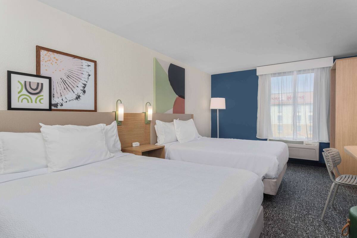 A hotel room with two beds, a desk, a chair, and artwork on the walls.