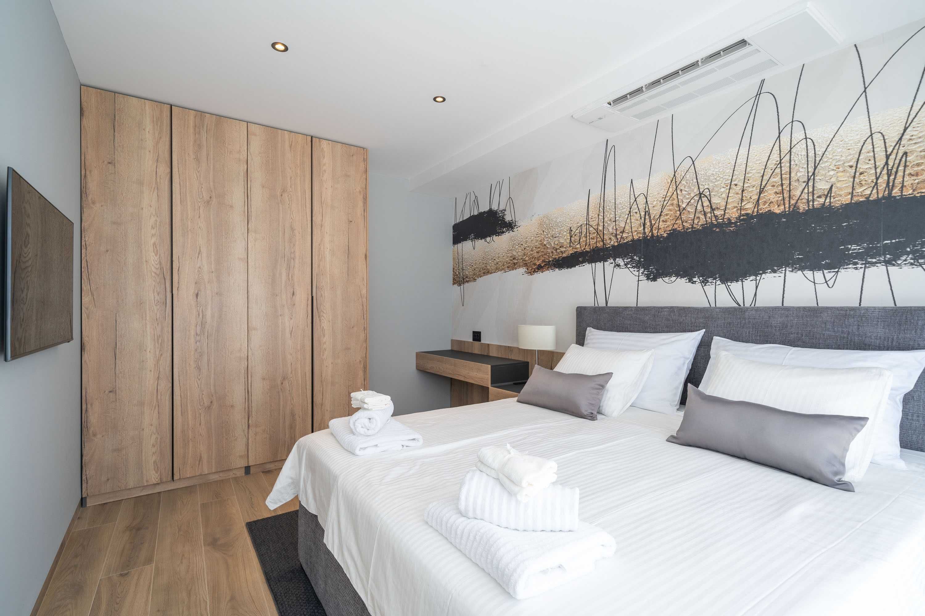 A modern hotel room with a large bed, wooden wardrobe, and a wall art depicting abstract lines and shapes.