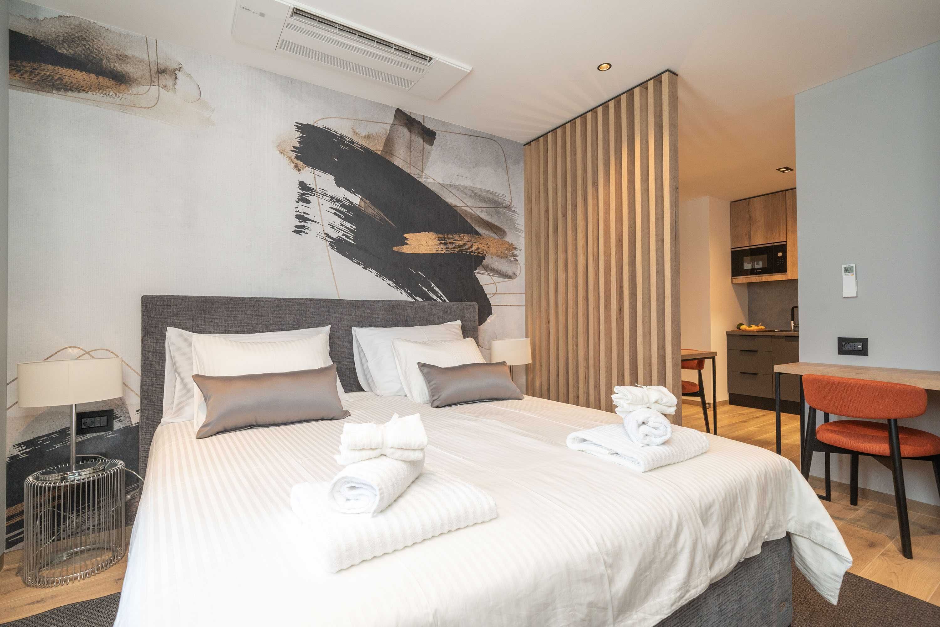A modern hotel room with a large bed, a desk, and a kitchenette.
