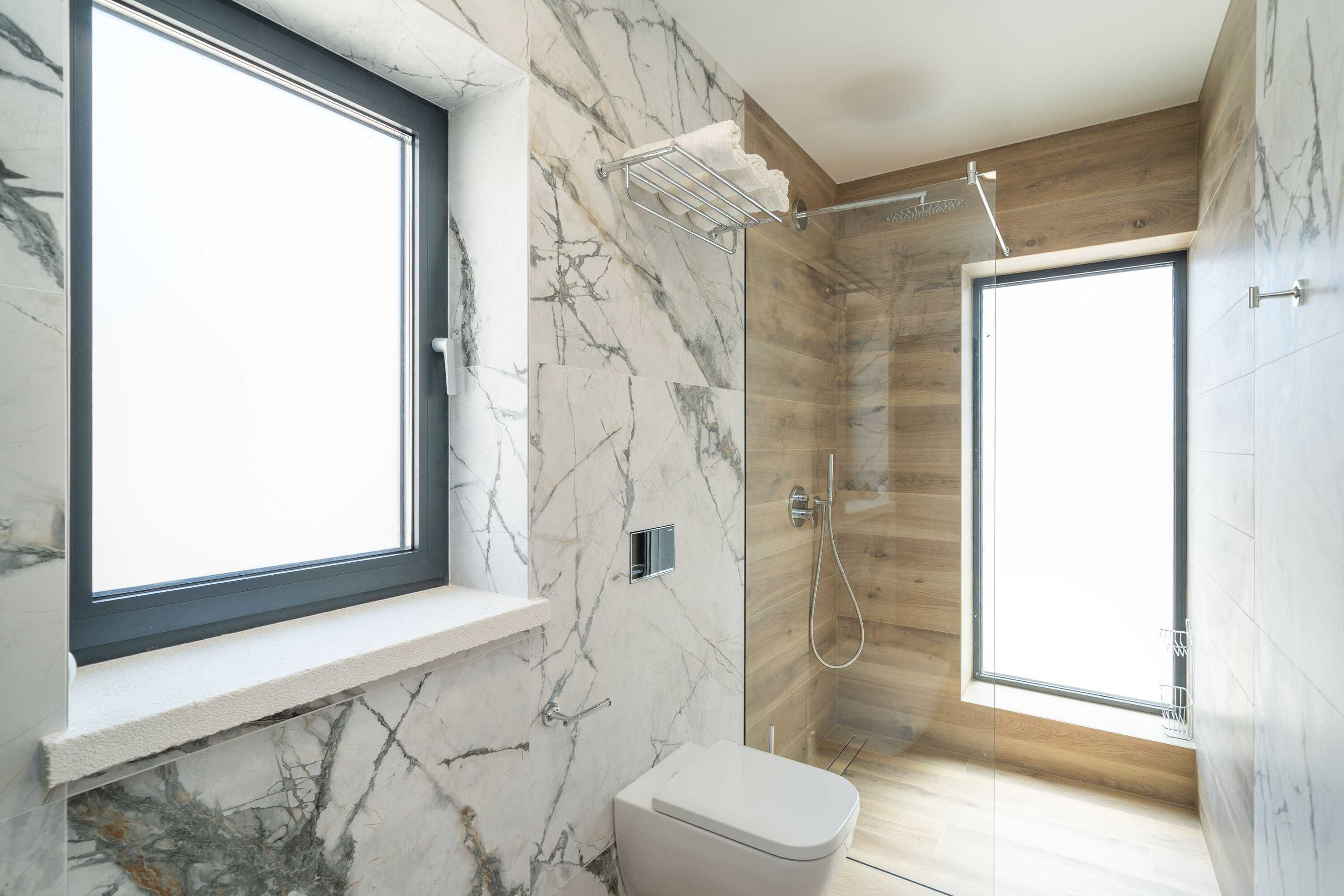 Un baño moderno con pared de mármol, ventana, ducha y retrete.