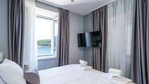 A hotel room with a bed, a TV mounted on the wall, and a window with curtains. - Apartments Villa Royale (Konavle)