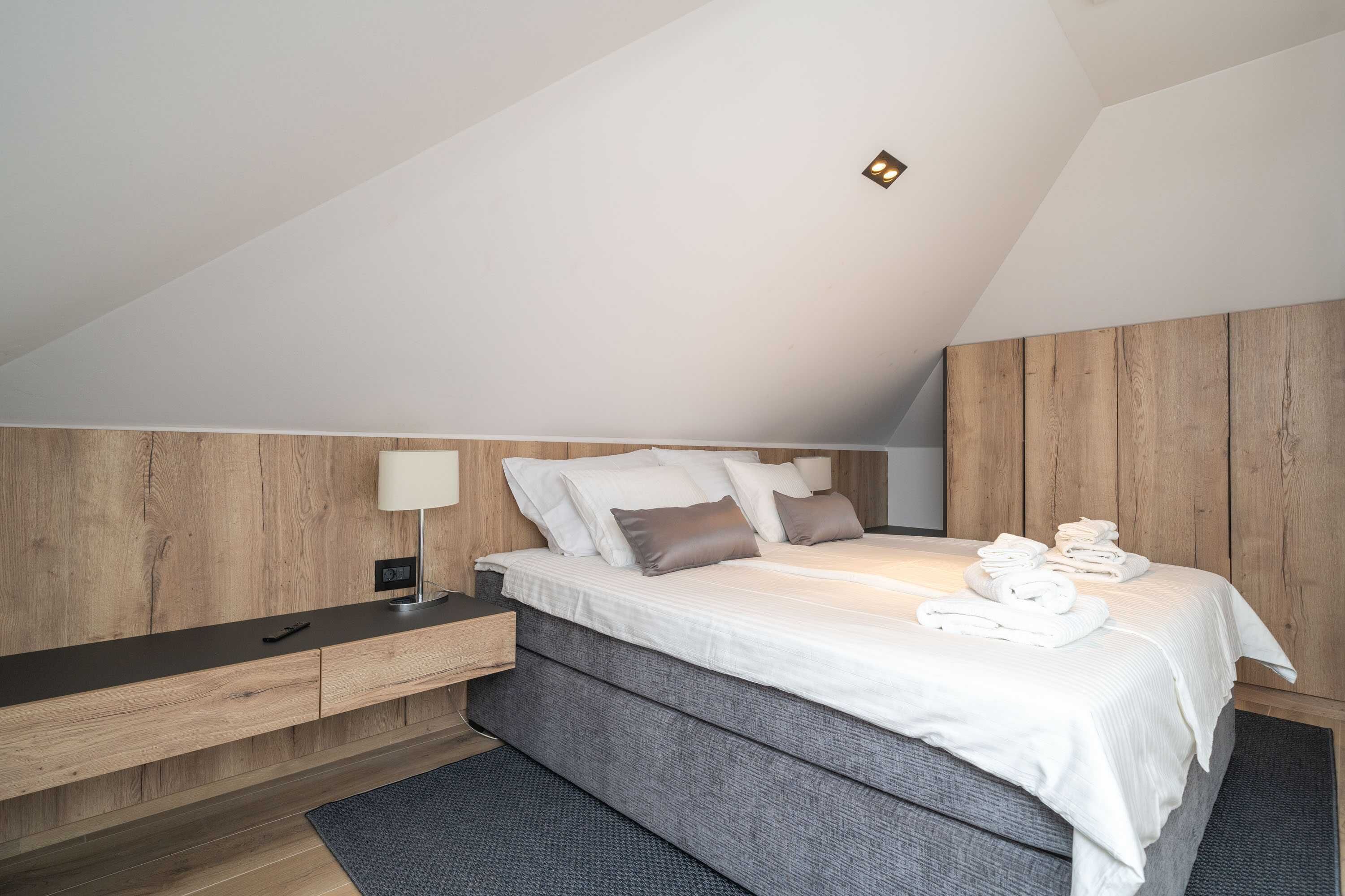 A modern bedroom with a sloped ceiling, a bed with white linens, a bedside table, and a nightstand.