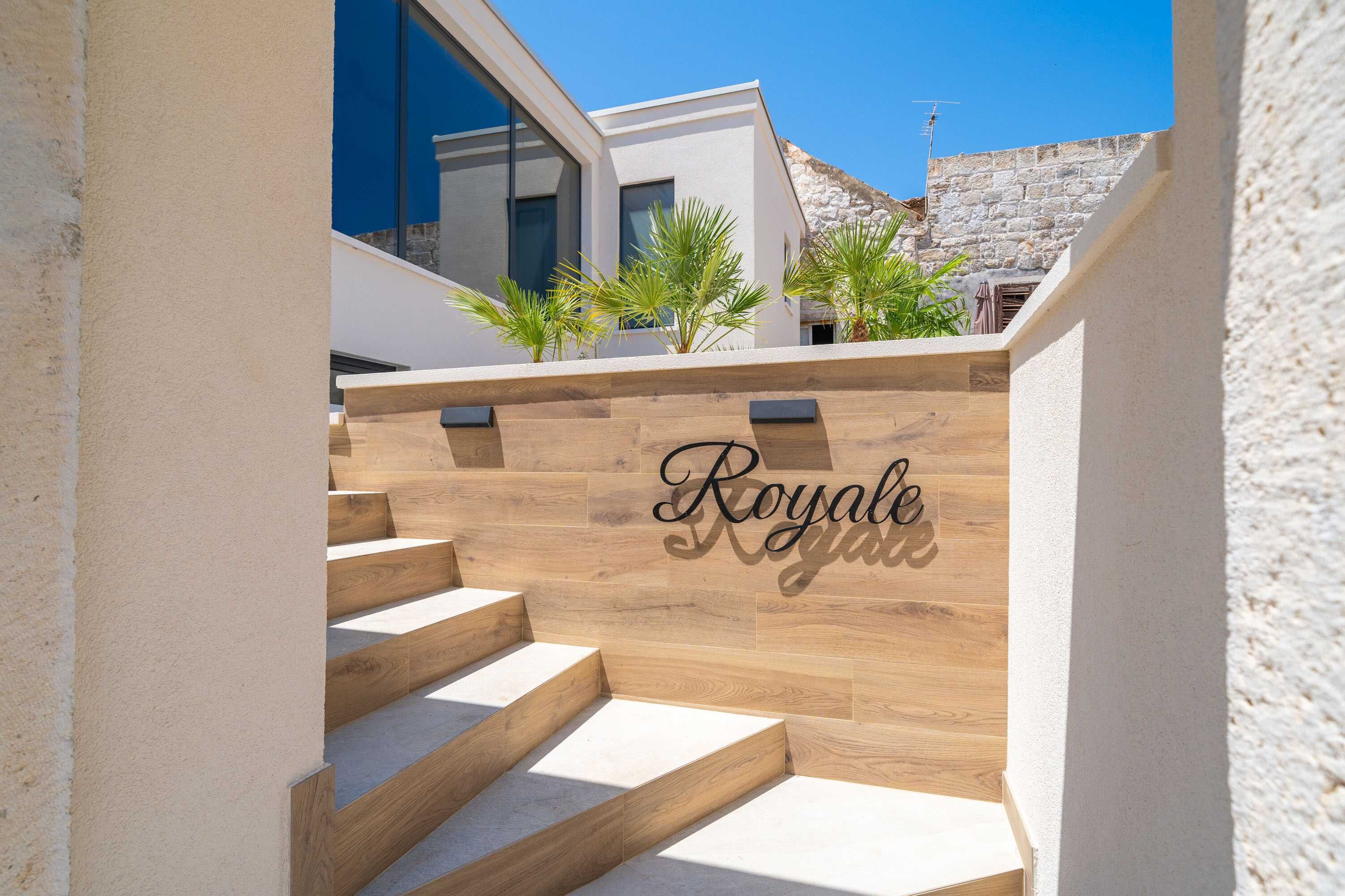 Een moderne trap met houten treden die leidt naar een witte muur met daarop het woord 'Royale' gegraveerd.
