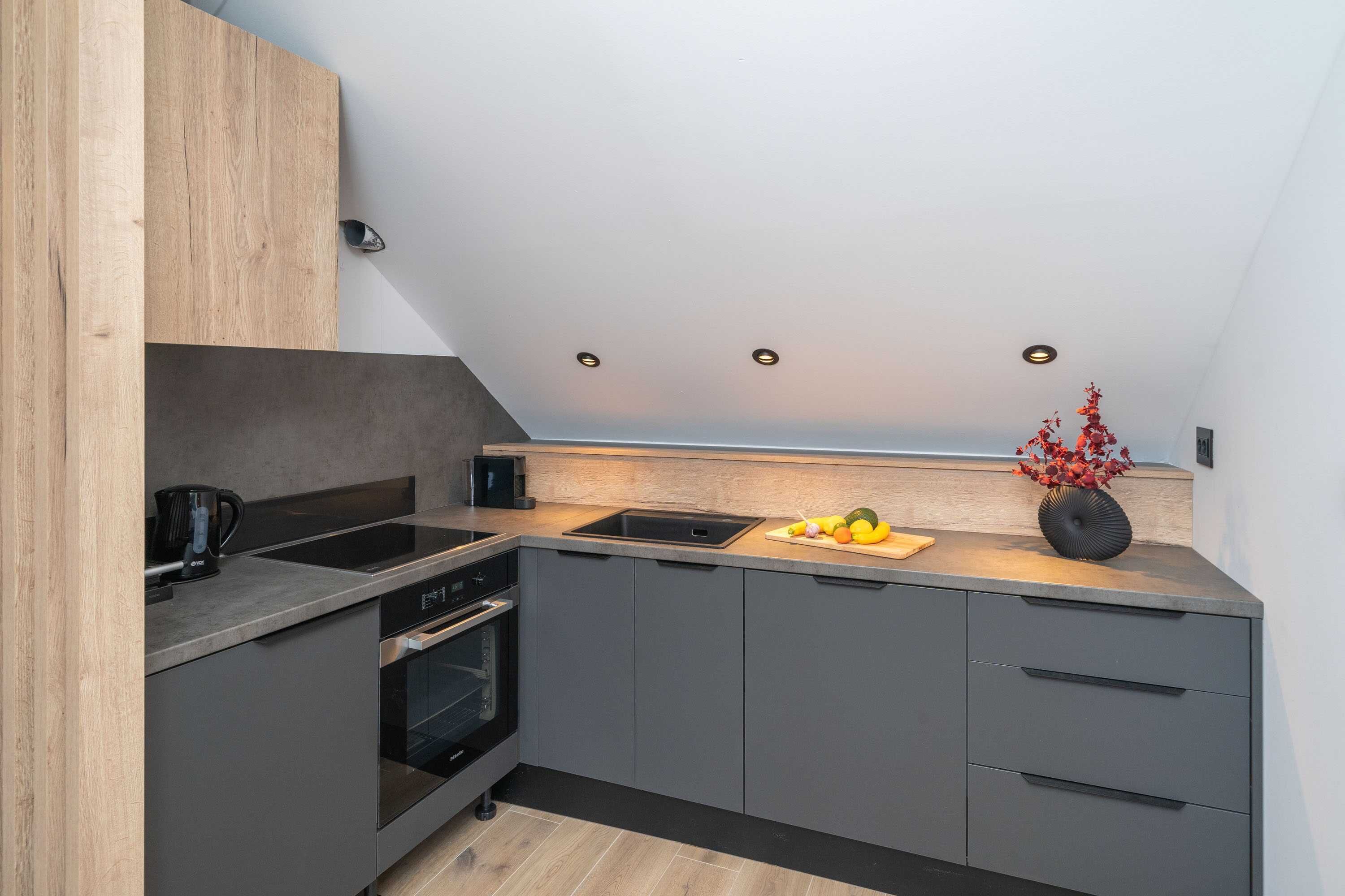 A modern kitchen with a built-in oven, a sink, and a countertop with a fruit bowl and vase.