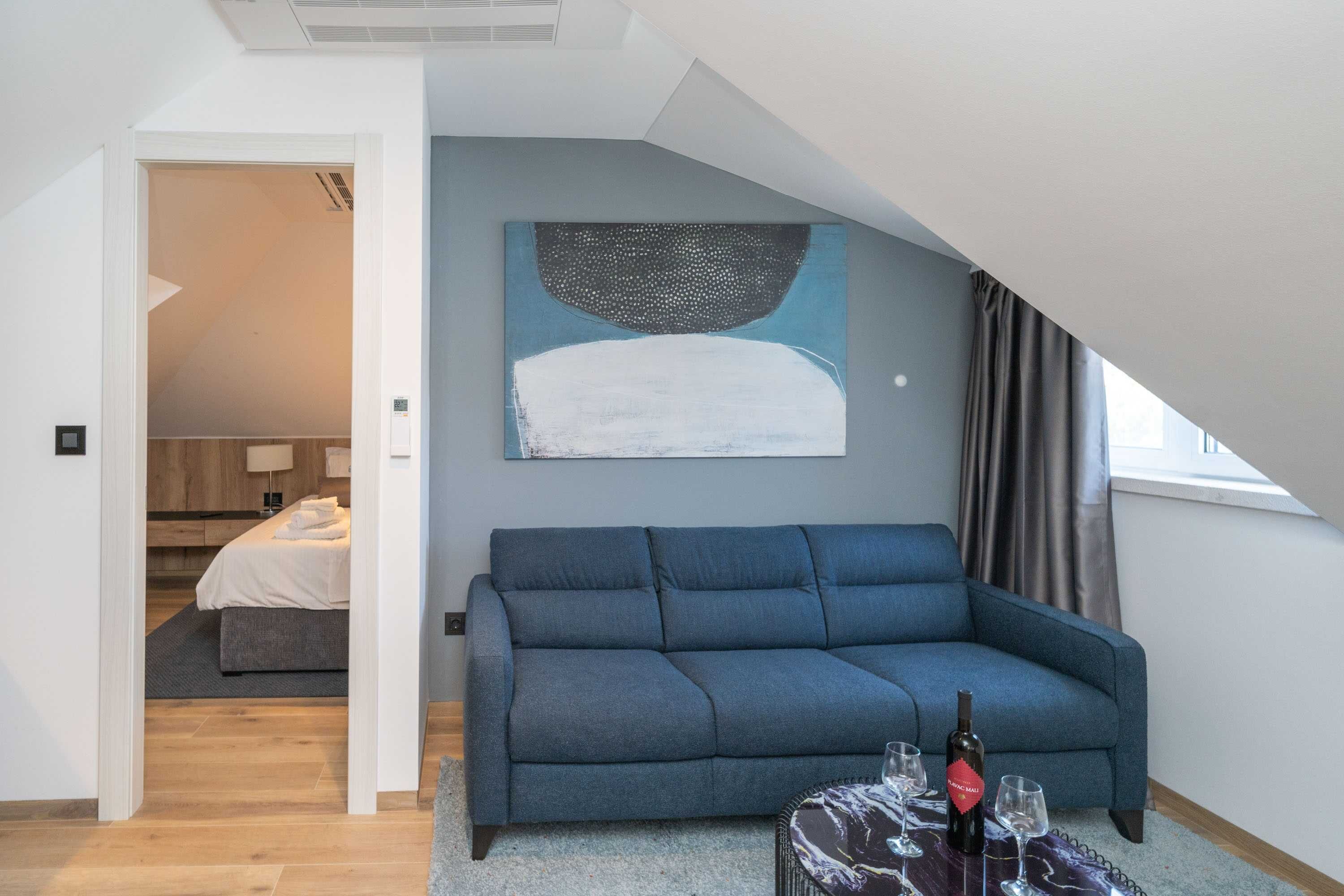 Ett modernt vardagsrum med en blå soffa, en tavla på väggen och en vinflaska på ett bord.