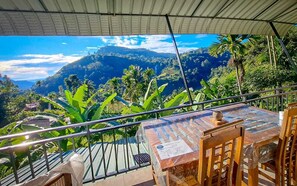 A terrace with a table and chairs, overlooking a mountainous landscape with lush greenery. - damil nishshanka (Ella)