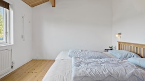 Una camera da letto con soffitto in legno, un letto con biancheria da letto bianca, un comodino con una lampada e una finestra con persiane.