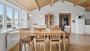 Un'ampia sala da pranzo con sedie in legno e un tavolo bianco, soffitto in legno e vista all'esterno attraverso ampie finestre.
