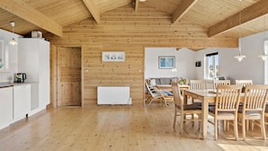 Un'ampia stanza con pavimento in legno, un'area pranzo con mobili in legno, un termosifone bianco e un soffitto con travi a vista.