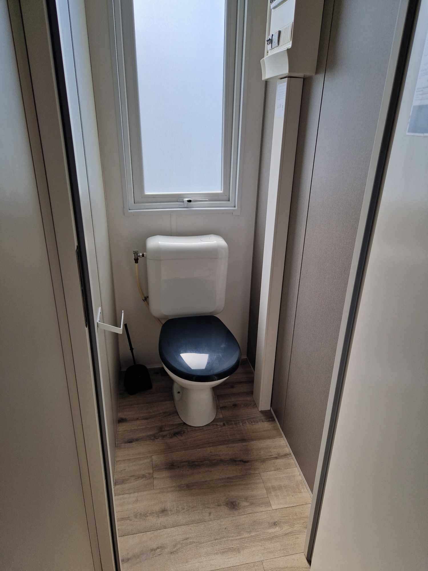 A compact bathroom with a toilet, a window, and a mop leaning against the wall.