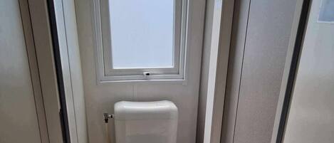 A compact bathroom with a toilet, a window, and a mop leaning against the wall.