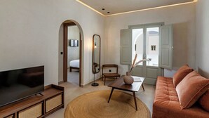 A modern living room with a flat-screen TV, a sofa, a coffee table, and a large woven rug. - Peranosa The Residency (Santorini)