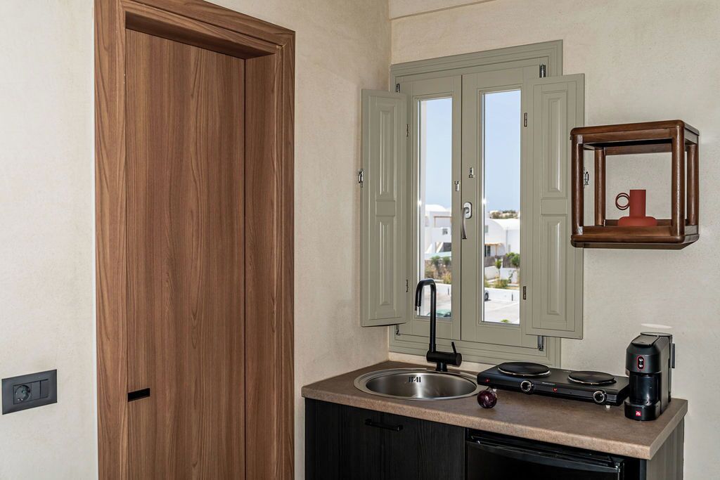 A compact kitchen with a wooden door, a window with green shutters, a sink, a stove, and a coffee maker.