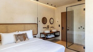 A modern hotel room with a large bed, a glass-enclosed shower, and a wooden vanity with two sinks. - Peranosa The Residency (Santorini)