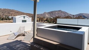 A rooftop terrace with a hot tub, lounge chairs, and a view of mountains. - Peranosa The Residency (Santorini)