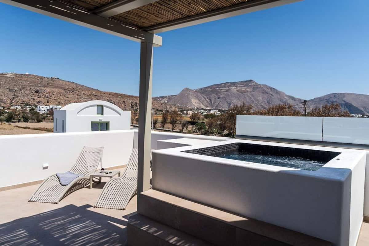 A rooftop terrace with a hot tub, lounge chairs, and a view of mountains.