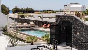 A pool area with lounge chairs, a stone wall, and a view of the sea. - Peranosa The Residency (Santorini)