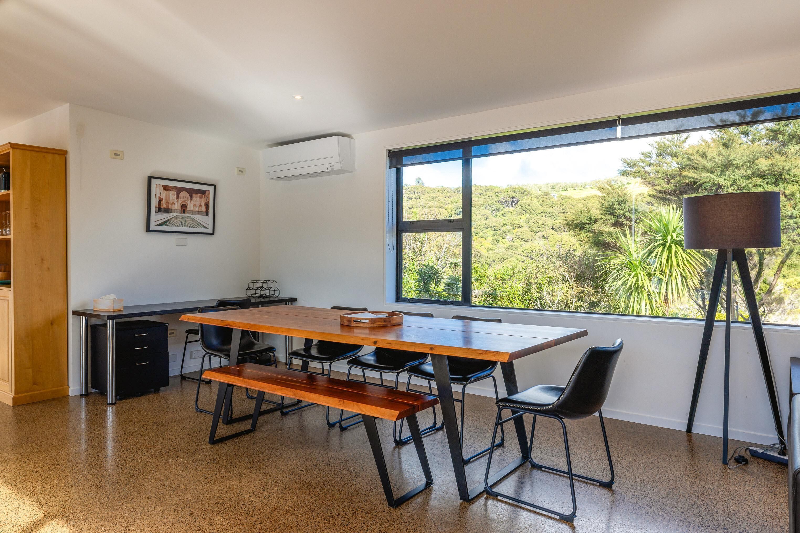 A modern room with a large window, a wooden table, black chairs, a desk, and a bookshelf.