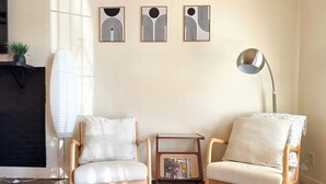 A room with two wooden chairs, a small table, and a floor lamp. There are three framed artworks on the wall. - Mid-Century Modern retreat (Visalia)