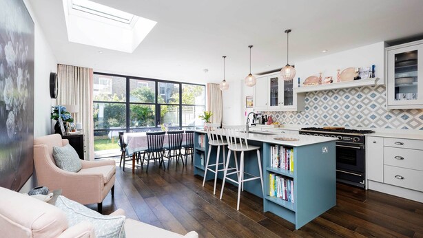 A modern kitchen with a central island, bar stools, and a dining area with a table and chairs. - Sunlit Symphony, by Veeve (London)