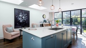 A modern kitchen with a large island, pendant lights, and a view of the outdoors through large windows. - Sunlit Symphony, by Veeve (London)
