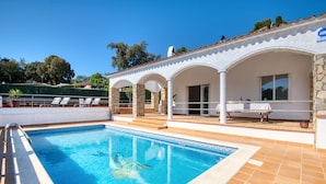A swimming pool with a stone deck, a covered seating area, and a view of the surrounding landscape.
