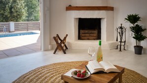 A cozy room with a fireplace, a dining table with a book and strawberries, and a view of a pool outside.